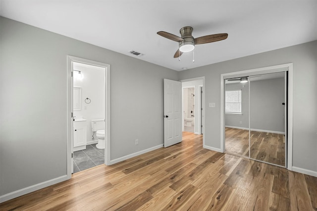 unfurnished bedroom featuring hardwood / wood-style floors, connected bathroom, a closet, and ceiling fan