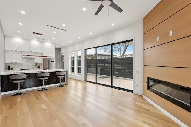 kitchen with stainless steel fridge, light hardwood / wood-style flooring, a kitchen breakfast bar, tasteful backsplash, and white cabinets