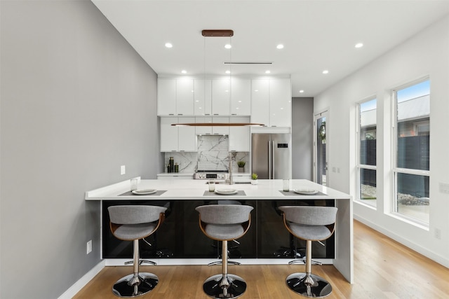 kitchen featuring backsplash, white cabinets, a kitchen bar, kitchen peninsula, and stainless steel appliances