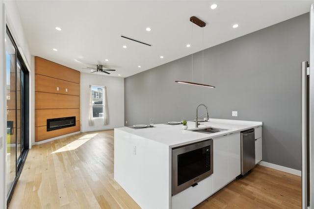 kitchen with pendant lighting, built in microwave, sink, a large fireplace, and light hardwood / wood-style flooring