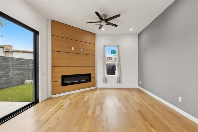 unfurnished living room featuring ceiling fan, a large fireplace, and light hardwood / wood-style flooring