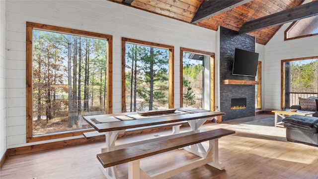 dining area with light wood-type flooring, lofted ceiling with beams, a stone fireplace, and a healthy amount of sunlight