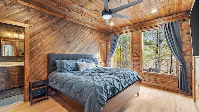 bedroom featuring multiple windows, wooden walls, light hardwood / wood-style flooring, and ensuite bath