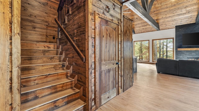 staircase featuring beamed ceiling, high vaulted ceiling, wood-type flooring, and wooden walls