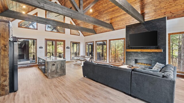 living room featuring beam ceiling, a stone fireplace, plenty of natural light, and high vaulted ceiling