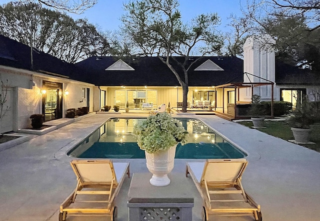 pool at dusk with a patio area and an outdoor pool