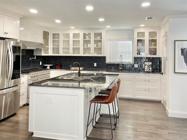 kitchen featuring white cabinetry, sink, dark stone counters, a kitchen island with sink, and appliances with stainless steel finishes