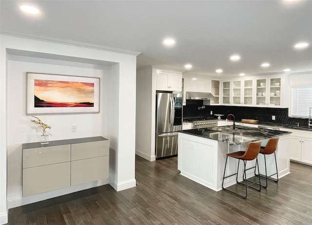 kitchen featuring stainless steel fridge, backsplash, a center island with sink, white cabinets, and a breakfast bar area