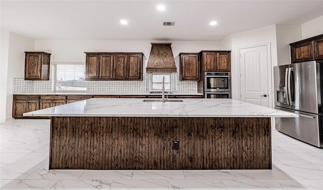 kitchen with dark brown cabinetry, sink, a center island with sink, appliances with stainless steel finishes, and decorative backsplash