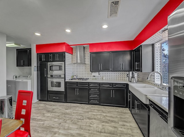 kitchen featuring washer / dryer, sink, light hardwood / wood-style floors, stainless steel appliances, and wall chimney range hood