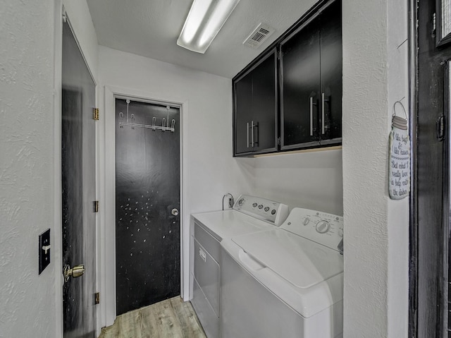 clothes washing area with washer and clothes dryer, cabinets, a textured ceiling, and light wood-type flooring