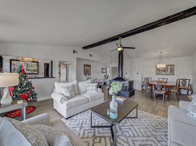 living room with lofted ceiling with beams, light wood-type flooring, a wood stove, and ceiling fan with notable chandelier