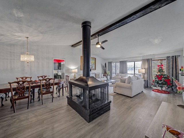 living room with light wood-type flooring, lofted ceiling with beams, a wood stove, and ceiling fan with notable chandelier