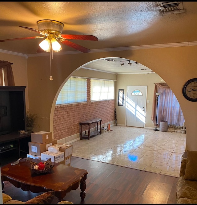 living room with crown molding, a textured ceiling, light hardwood / wood-style flooring, ceiling fan, and brick wall