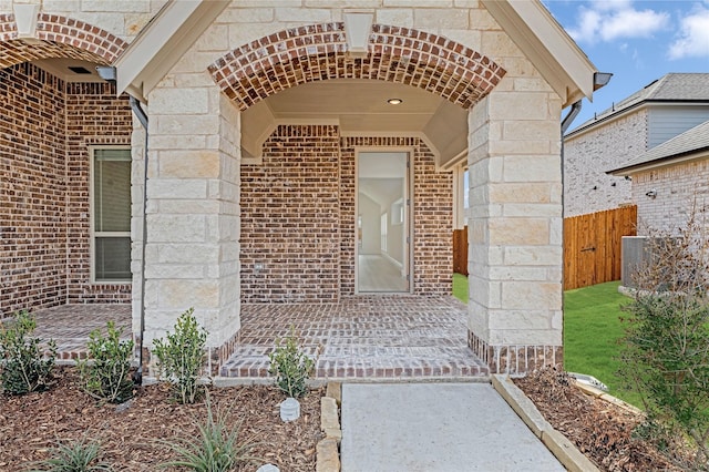 entrance to property with stone siding, brick siding, and fence