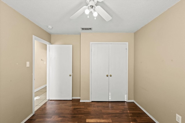 unfurnished bedroom with ceiling fan, a textured ceiling, dark hardwood / wood-style flooring, and a closet