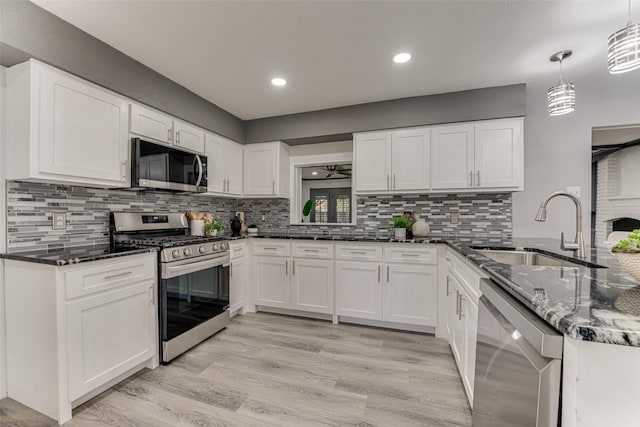5503 Pecan Grove Dr, Sachse, TX 75048 - kitchen featuring appliances with stainless steel finishes, a sink, white cabinetry, dark stone countertops, and light wood finished floors