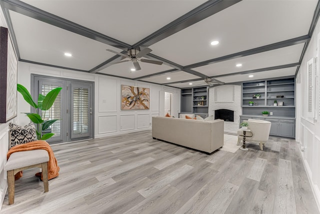 living room featuring built in shelves, ceiling fan, beamed ceiling, a fireplace, and light hardwood / wood-style floors