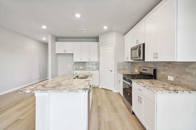 kitchen featuring light wood-type flooring, stainless steel appliances, a kitchen island with sink, sink, and white cabinetry