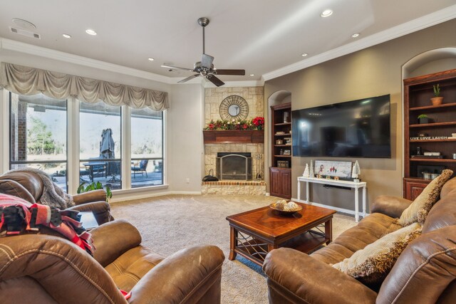 carpeted living room featuring a stone fireplace, crown molding, built in features, and ceiling fan