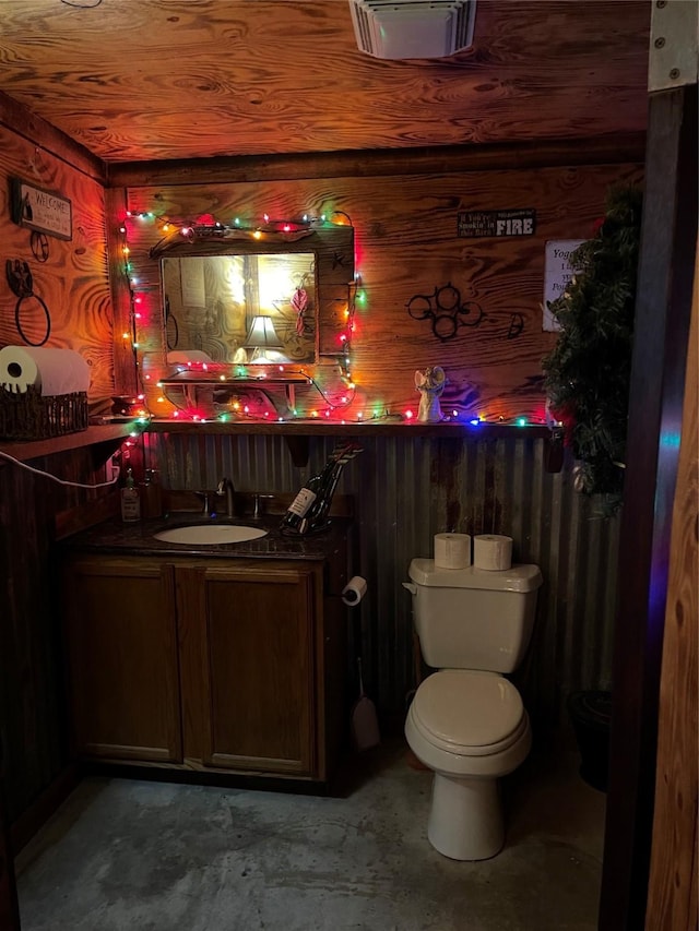 bathroom featuring vanity, toilet, concrete floors, and wooden walls