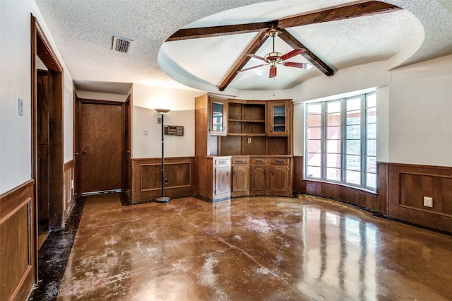 unfurnished living room with beam ceiling, ceiling fan, wood walls, and a textured ceiling