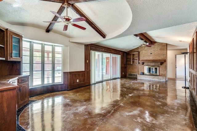 unfurnished living room with wood walls, lofted ceiling with beams, a textured ceiling, and a brick fireplace