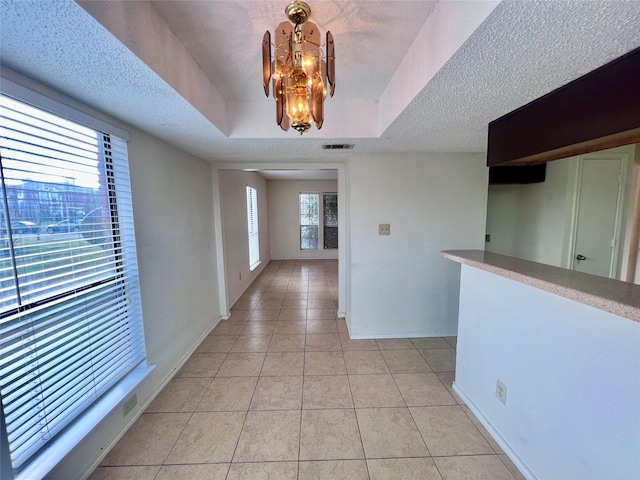 hallway with a wealth of natural light, light tile patterned floors, a textured ceiling, and an inviting chandelier