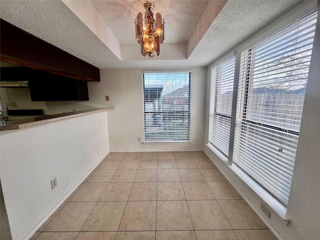 unfurnished dining area featuring light tile patterned floors, a textured ceiling, a tray ceiling, and a notable chandelier