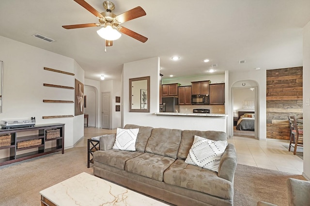 carpeted living room with ceiling fan and wood walls