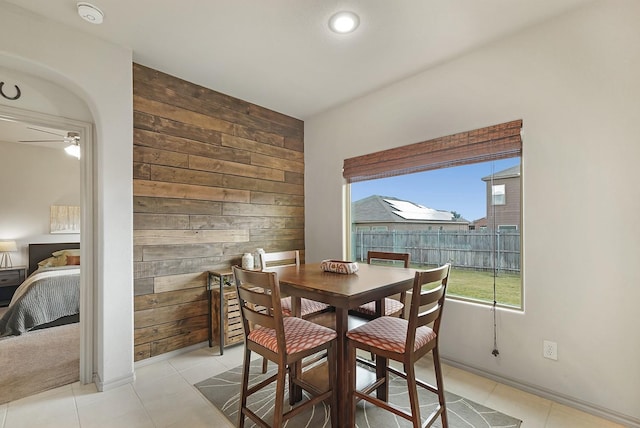 dining area featuring light tile patterned floors, ceiling fan, and wooden walls