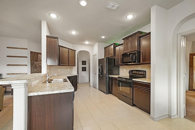 kitchen featuring black appliances, sink, light tile patterned floors, dark brown cabinets, and a kitchen bar