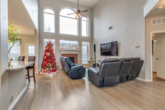 living room with ceiling fan, light wood-type flooring, a towering ceiling, and a fireplace