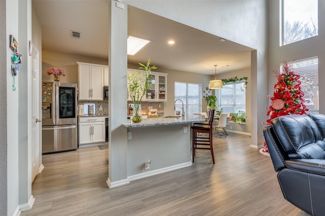 kitchen featuring white cabinetry, light stone counters, stainless steel refrigerator with ice dispenser, a breakfast bar, and light wood-type flooring