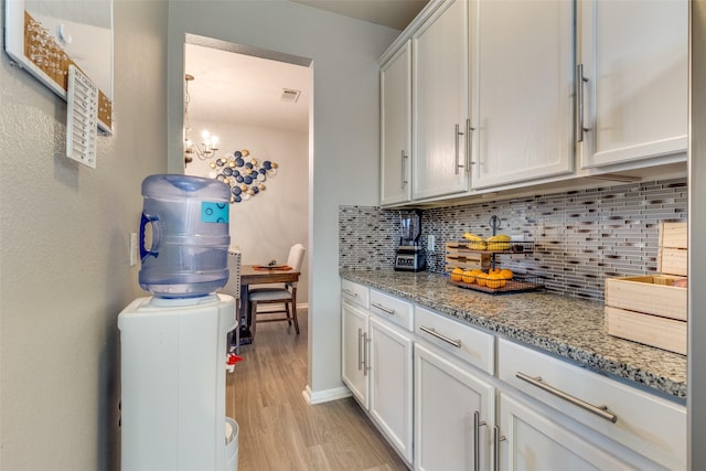 kitchen with white cabinetry, light stone countertops, a notable chandelier, decorative backsplash, and light wood-type flooring