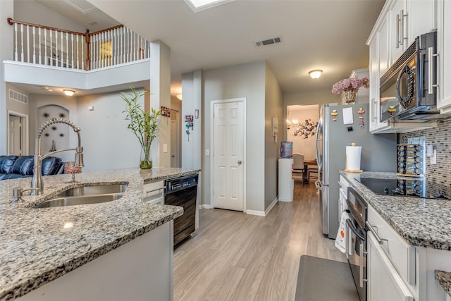 kitchen featuring black appliances, sink, light hardwood / wood-style flooring, light stone countertops, and white cabinetry