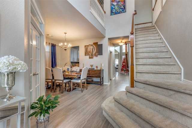 entryway with light hardwood / wood-style floors, french doors, a high ceiling, and an inviting chandelier