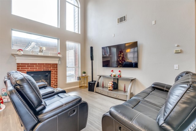 living room with a towering ceiling, light wood-type flooring, a wealth of natural light, and a brick fireplace