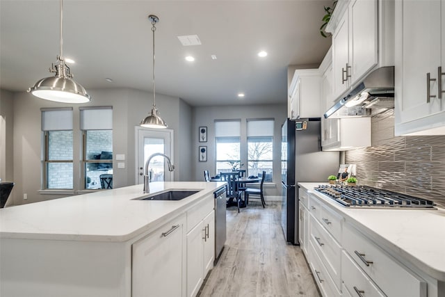 kitchen with a kitchen island with sink, sink, light wood-type flooring, decorative light fixtures, and white cabinetry