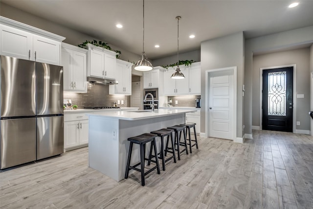 kitchen with white cabinetry, sink, stainless steel fridge, light hardwood / wood-style floors, and a kitchen island with sink