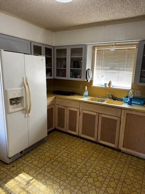 kitchen with a textured ceiling, white fridge with ice dispenser, and sink