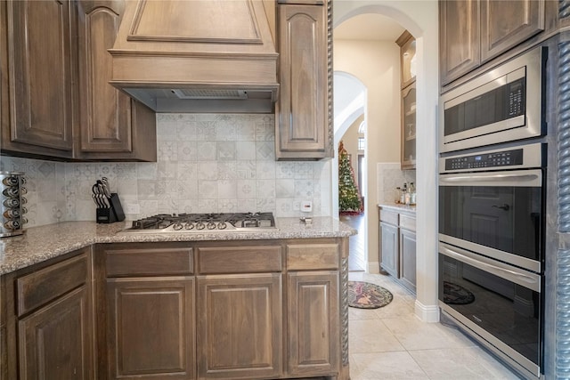 kitchen with premium range hood, decorative backsplash, stainless steel appliances, and light stone counters