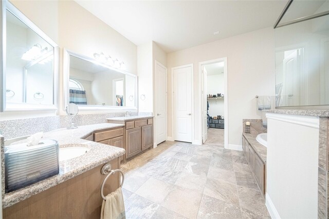 full bath featuring a bathtub, a sink, baseboards, and two vanities