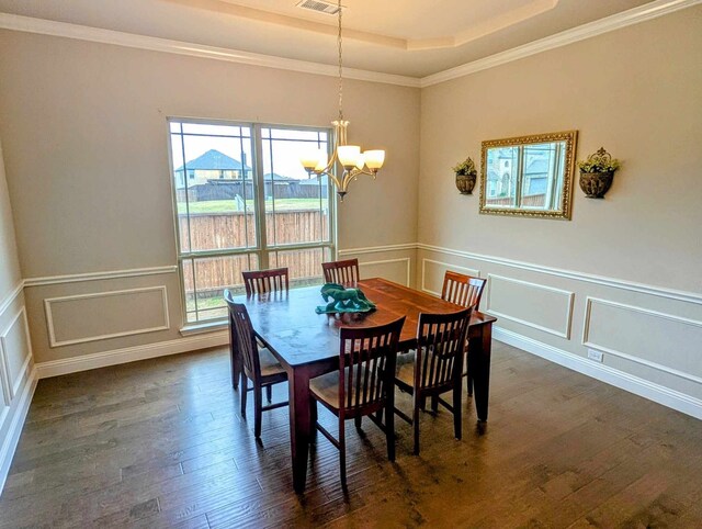 dining area featuring visible vents, a tray ceiling, dark wood-style flooring, a decorative wall, and a notable chandelier