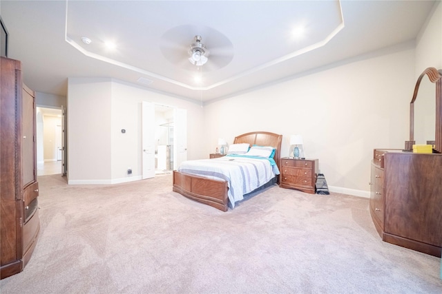 bedroom with ceiling fan, a raised ceiling, ensuite bathroom, and light carpet