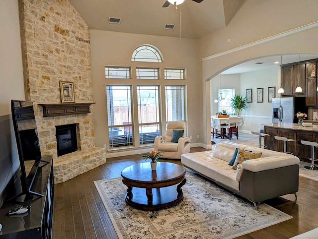 living room featuring arched walkways, visible vents, a stone fireplace, and dark wood-style floors