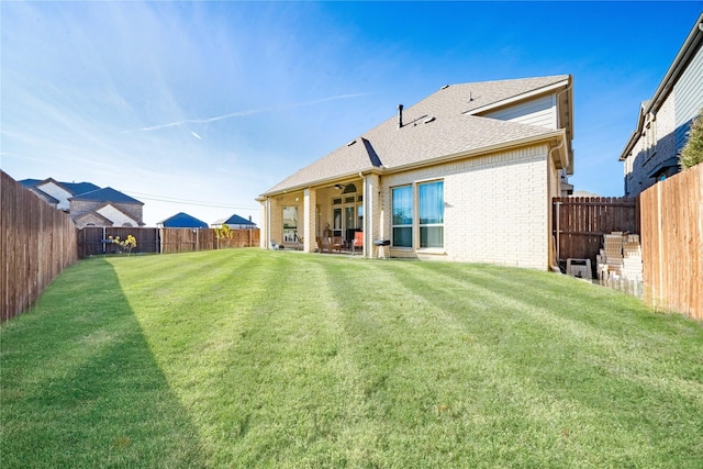 rear view of house featuring brick siding, ceiling fan, roof with shingles, a lawn, and a fenced backyard