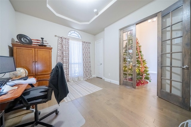 office area with light hardwood / wood-style flooring and a tray ceiling