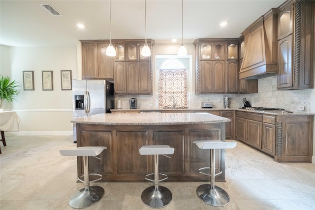 kitchen with visible vents, a kitchen island, custom range hood, glass insert cabinets, and tasteful backsplash