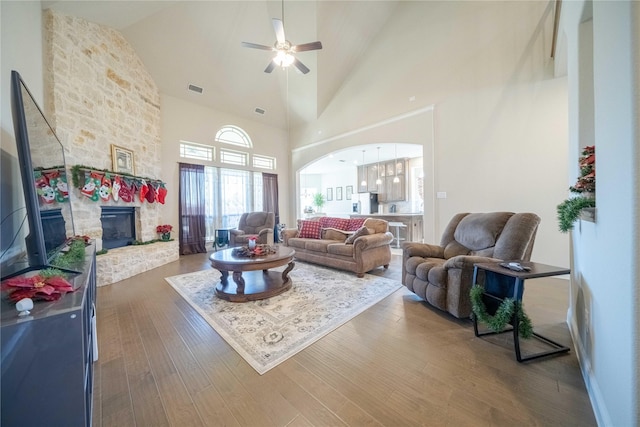 living room featuring dark hardwood / wood-style floors, ceiling fan, a stone fireplace, and high vaulted ceiling